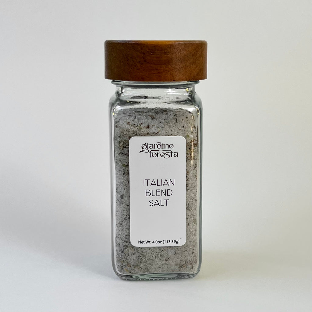 A clear glass spice jar filled with seasoning salt, featuring a white label with the brand name 'Giardino Foresta' and a dark brown wooden lid, set against a plain white background.