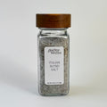 A clear glass spice jar filled with seasoning salt, featuring a white label with the brand name 'Giardino Foresta' and a dark brown wooden lid, set against a plain white background.