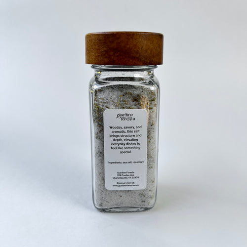 A clear glass spice jar filled with seasoning salt, featuring a natural brown wooden lid and a white label against a white background.