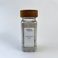 A square glass spice jar filled with seasoning salt, featuring a white label with the brand name 'Giardino Foresta' and a dark brown wooden lid, set against a white background.