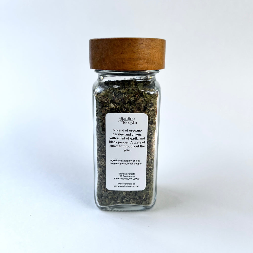 A clear glass spice jar filled with dried herbs, topped with a natural wood lid, and featuring a white label.